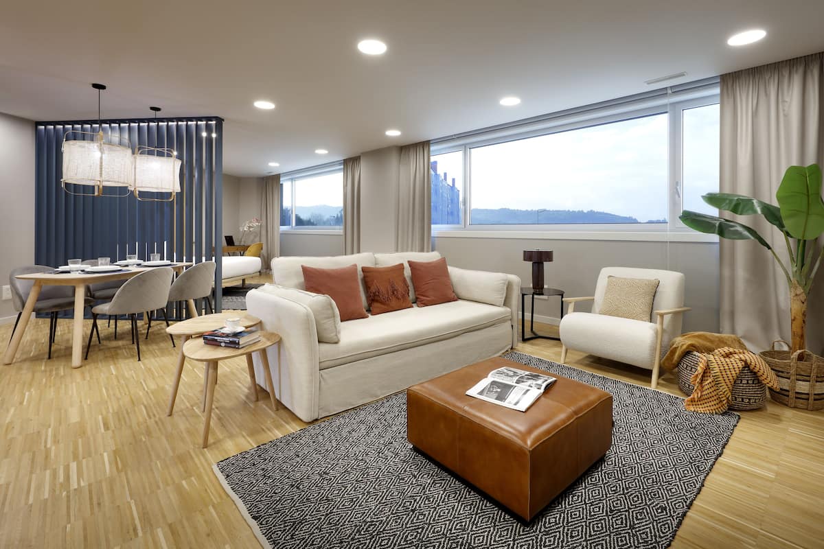 A modern living room with a sofa, ottoman, and dining area.