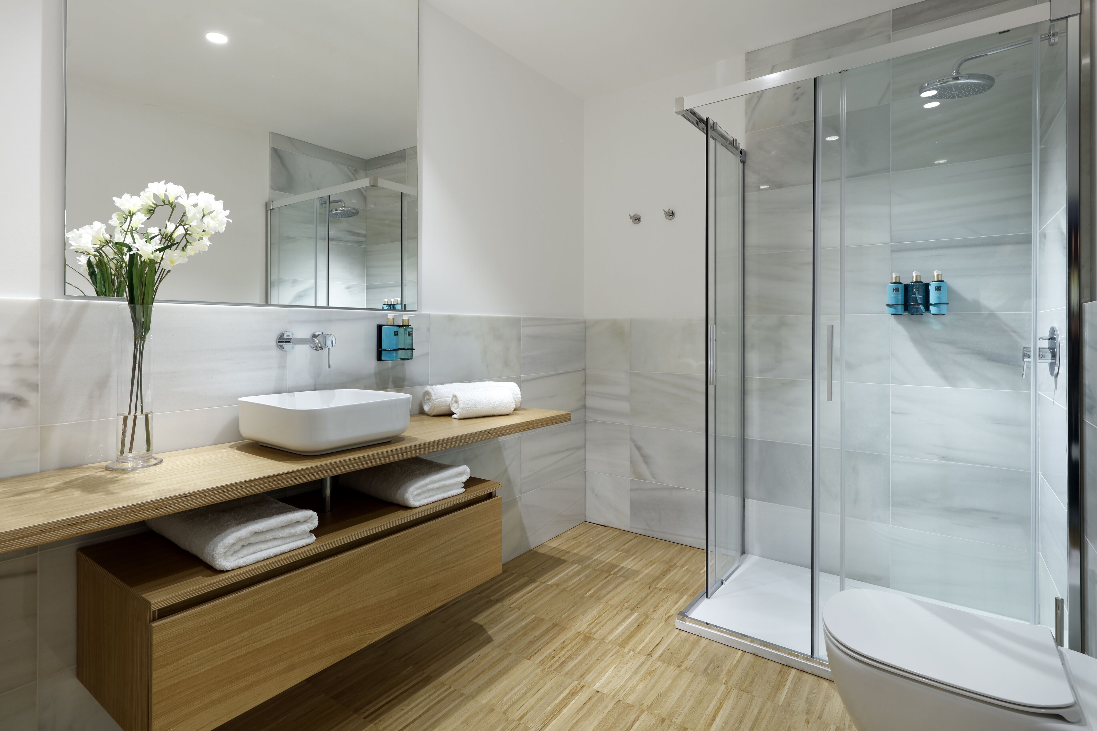 Een moderne badkamer met een douchecabine van glas, een houten wastafelmeubel met een witte wasbak en een grote spiegel.