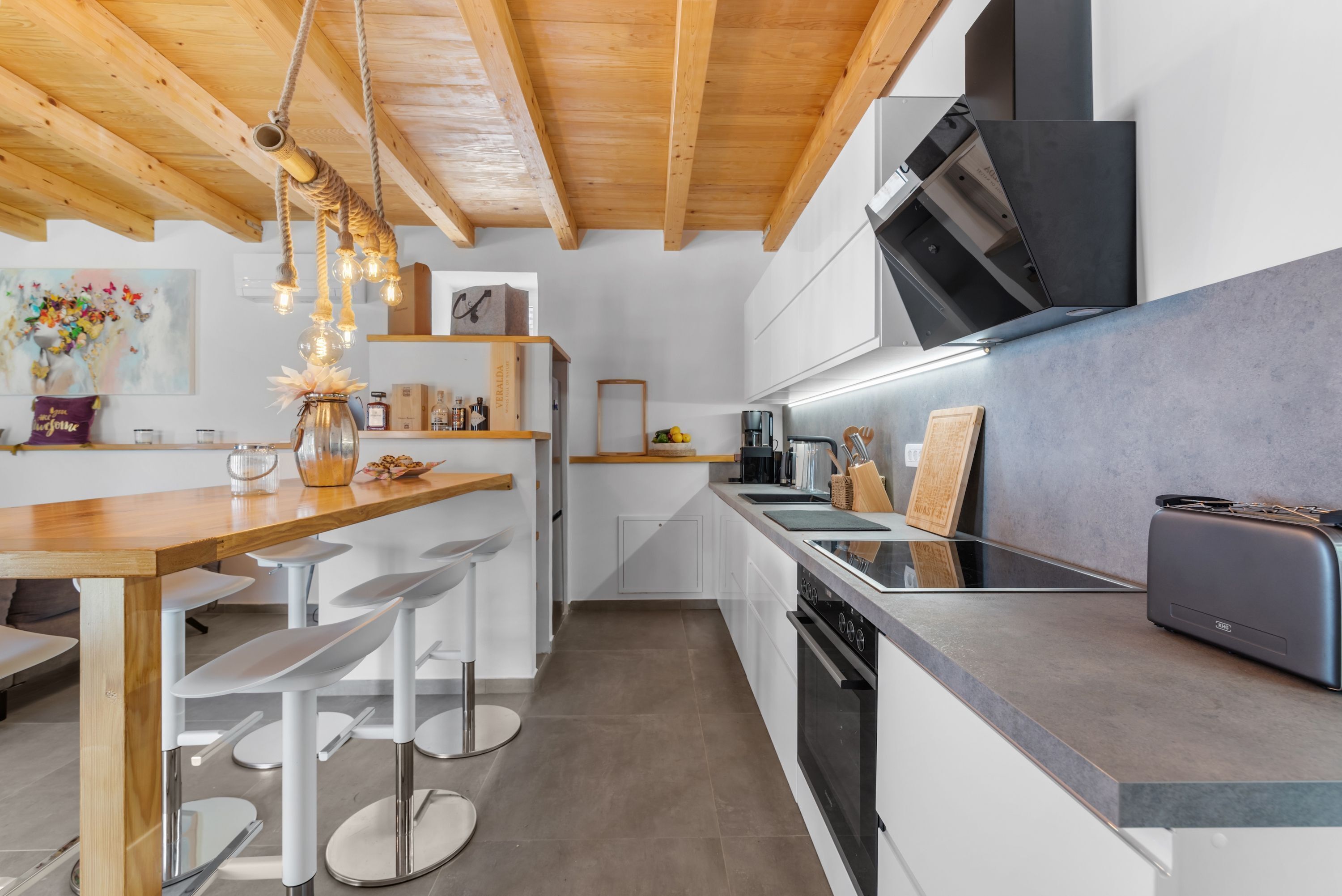 Eine moderne Küche mit Holzbalken, weißen Schränken und einer Bar mit Sitzgelegenheiten.
