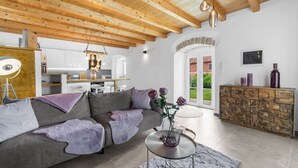 A modern living room with a grey sofa, a coffee table, and a vase with flowers. There is a wooden cabinet with alphabet letters and a stone archway leading to a balcony. - Lavova in Brtonigla With 3 Bedrooms and 2 Bathrooms (Brtonigla)