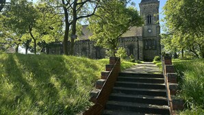 En kirke med et tårn og et ur, omgivet af træer og en græsplæne med en murstens trappe op til indgangen.