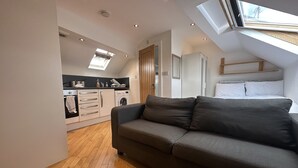 En moderne lejlighed i loftstil med skråvæg, indbygget køkken, en gr å sofa og et ovenlys.