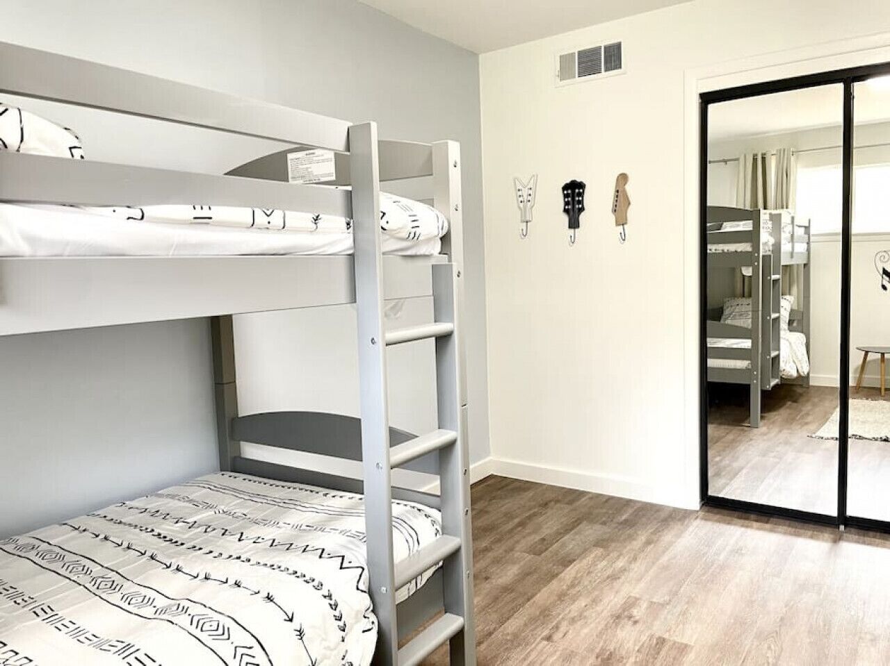 Une chambre avec des lits superposés, un plancher en bois, un mur blanc et une porte-fenêtre coulissante donnant sur une autre pièce.