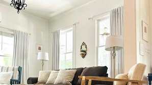 A living room with a dark grey sofa, two armchairs, a coffee table, and a chandelier. - Willow Suite at The Mockingbird Inn Boutique Hotel (Ocean Springs)