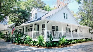 A white two-story house with a porch, surrounded by greenery and an American flag. - Willow Suite at The Mockingbird Inn Boutique Hotel (Ocean Springs)