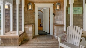 Une façade en bois avec un porche, une chaise en bois et une porte donnant sur l’intérieur.