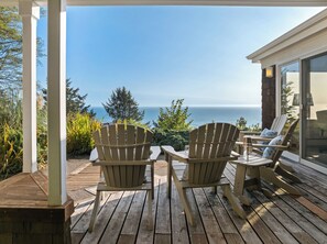 Una terraza de madera con dos sillas Adirondack mirando un hermoso panorama marino.