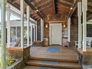 Une véranda en bois avec une entrée couverte, des sièges extérieurs et une porte donnant sur l’intérieur.