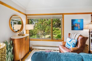 Ein Zimmer mit einem großen Fenster, einem Holzschrank, einem runden Spiegel, einem Gemälde und einem Ledersessel.