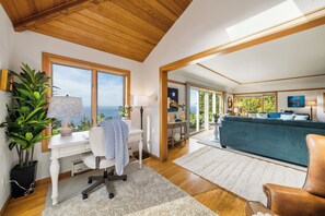 Un amplio salón con vista al mar, un escritorio con lámpara, un sofá y una silla.