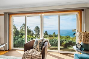 Ein Zimmer mit einer großen Schiebetür, die einen schönen Blick auf das Meer und Bäume freigibt.