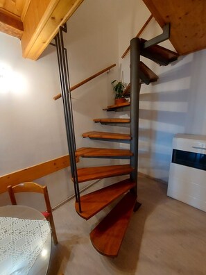 Un escalier en bois au design moderne, une chaise blanche et une table recouverte d’une nappe en dentelle.