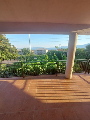 Un balcon doté d’un sol carrelé, d’une rambarde en métal et offrant une vue sur des bâtiments et de la verdure au loin.