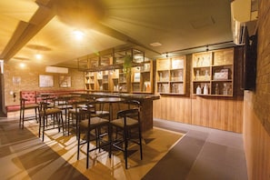 Um restaurante com área de bar, várias mesas e cadeiras, e prateleiras com garrafas e copos.