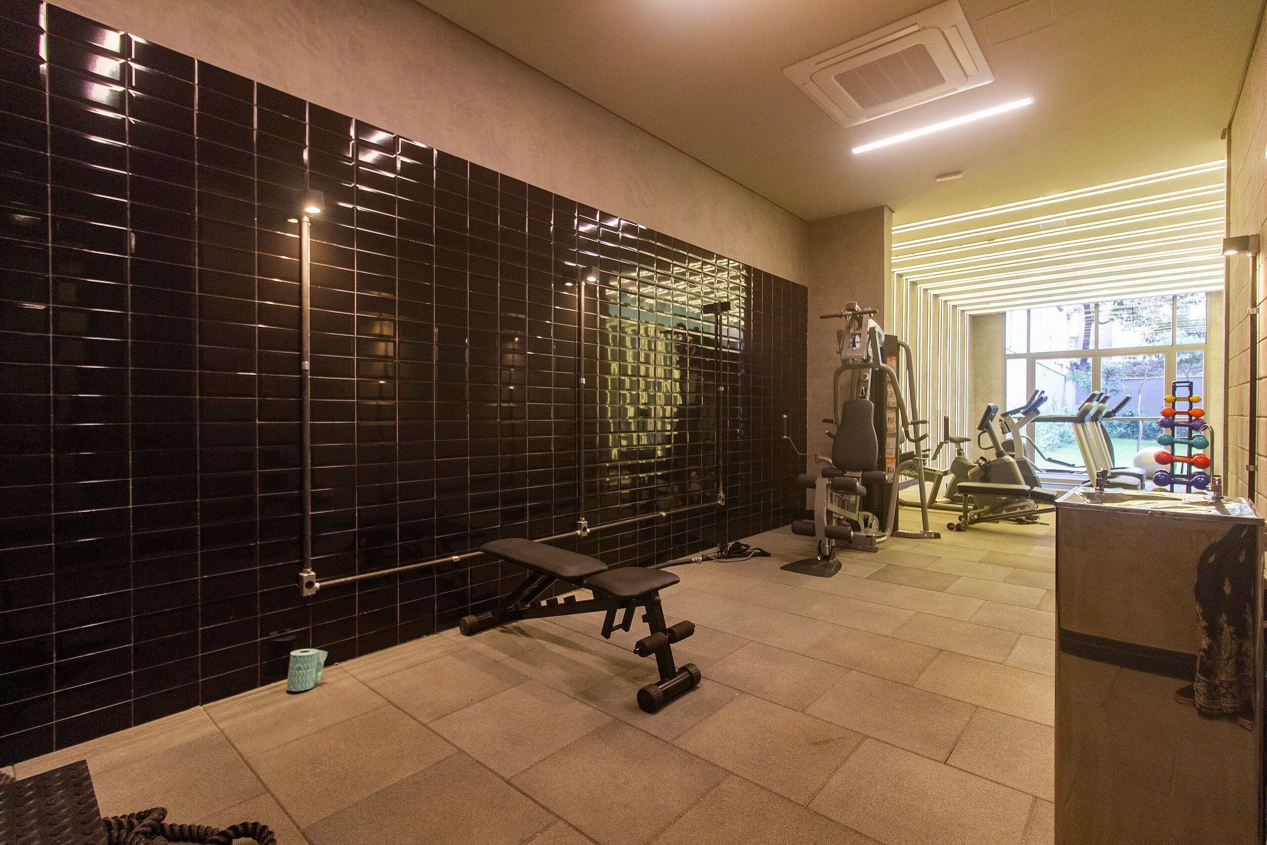 A gym with exercise equipment, a bench, and a wall of black tiles.