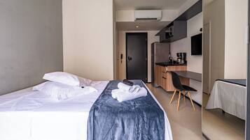 A hotel room with a bed, a desk, a chair, and a kitchenette.