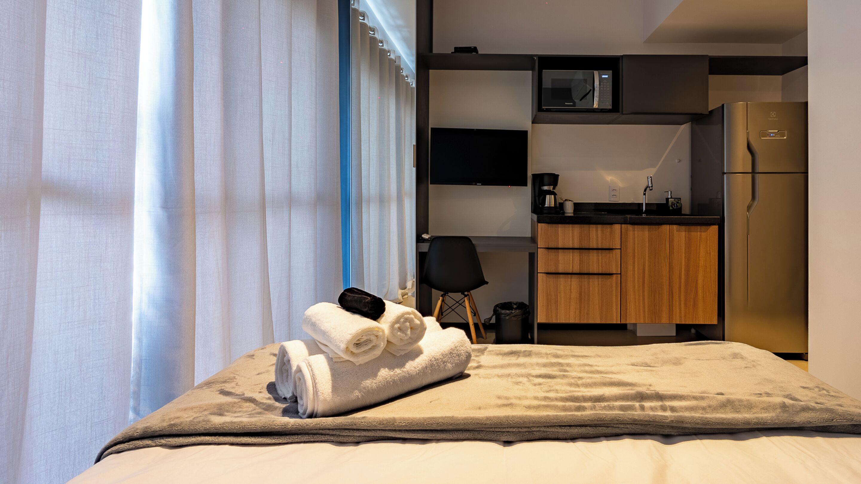 Een hotelkamer met een bed, een kitchenette met een magnetron, een koelkast en een raam met gordijnen.