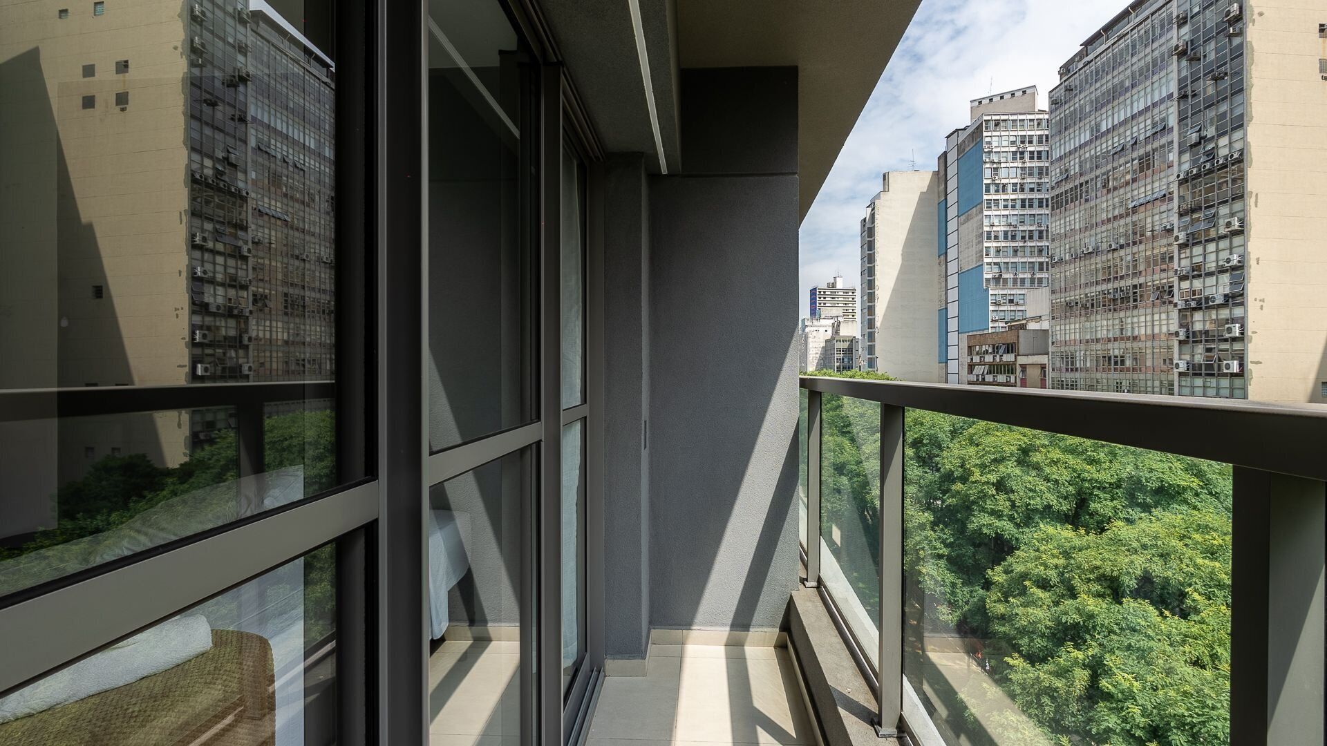 A balcony with a view of dense green trees and high-rise buildings.