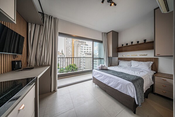A modern hotel room with a bed, bedside table, TV, and a balcony with a city view. - VN Consolação (São Paulo)