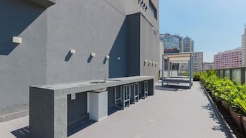 Un baño exterior moderno con lavamanos y estación de lavado de manos, un área de descanso cubierta y una hilera de plantas en macetas.