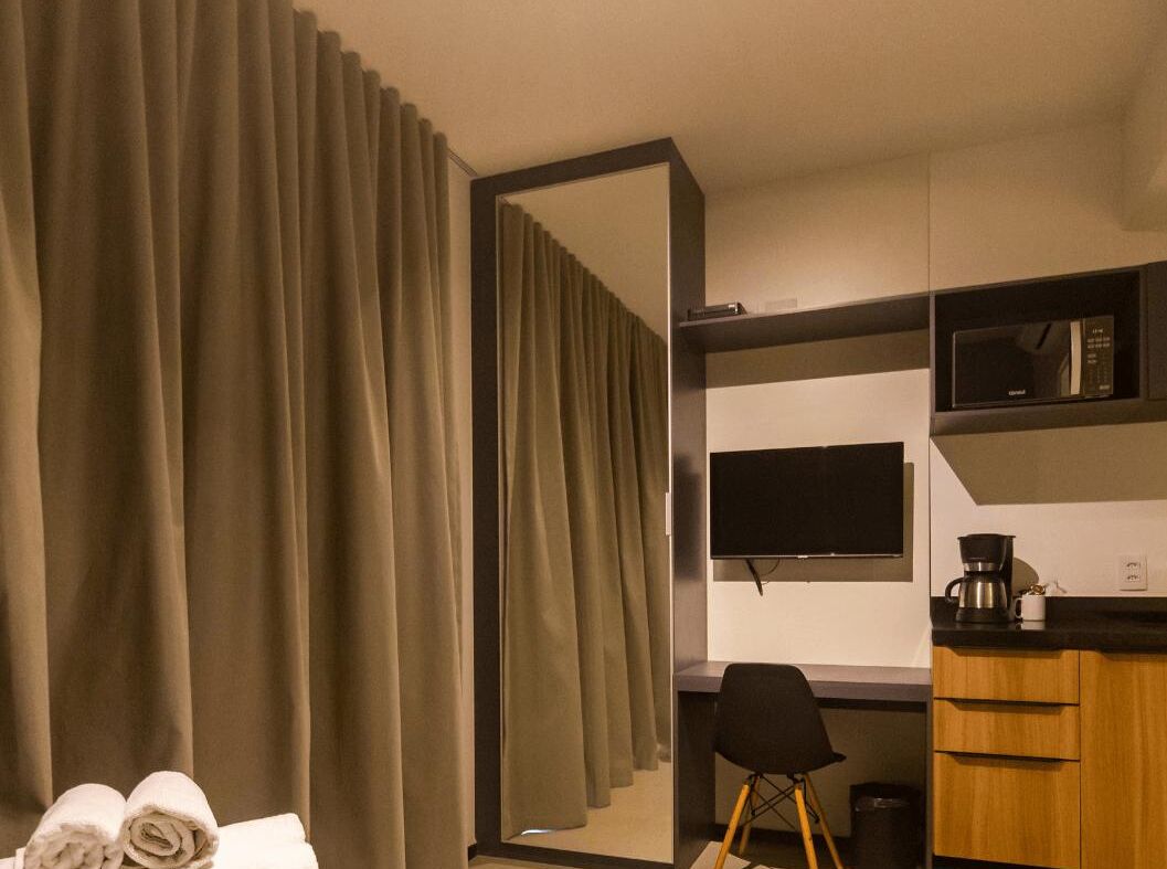 Habitación de hotel con un espejo grande, un televisor de pantalla plana, microondas, cafetera y un escritorio con silla.