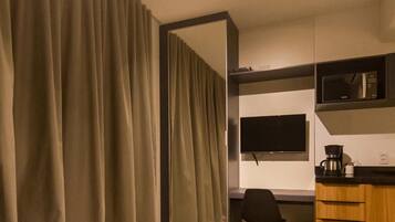 Habitación de hotel con un espejo grande, un televisor de pantalla plana, microondas, cafetera y un escritorio con silla.