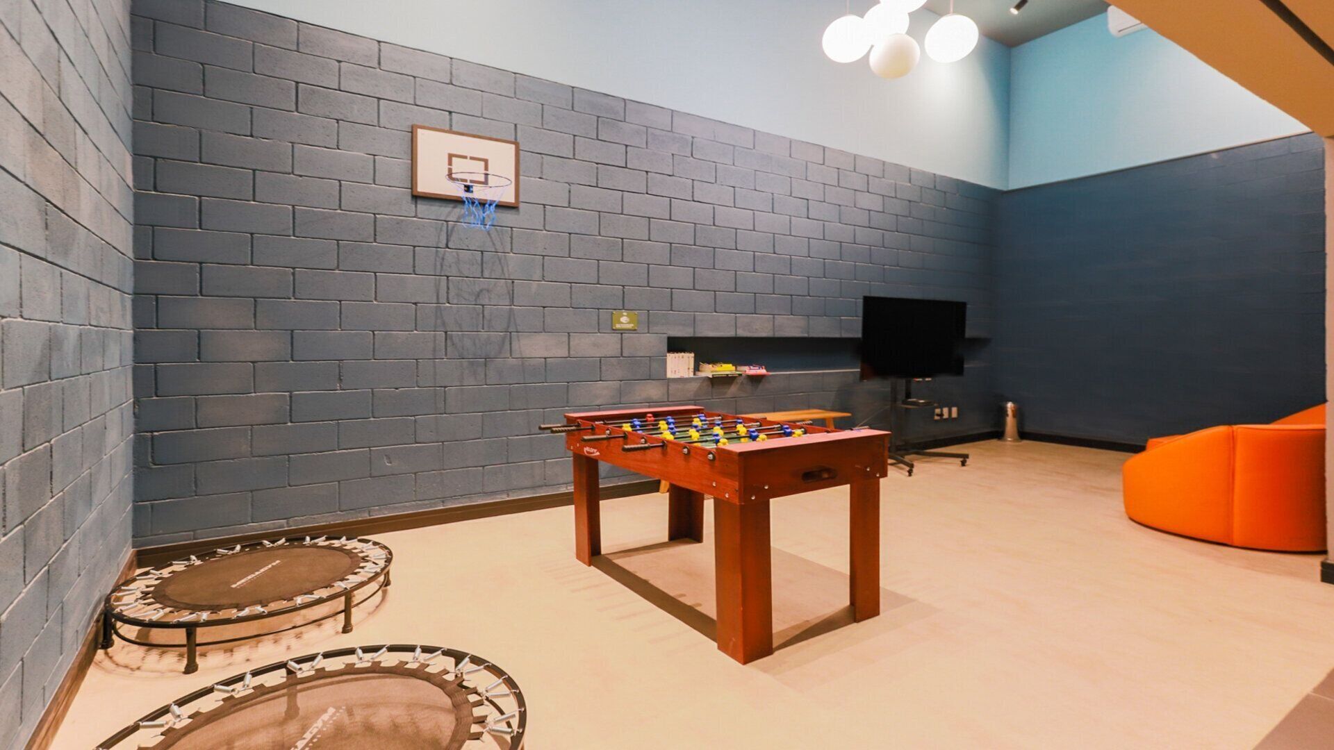 Ein Zimmer mit einer Fußballtischkicker, einem kleinen Basketballkorb, einem Fernseher und einem Trampolin.