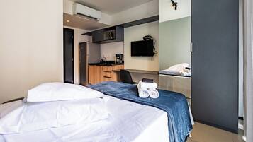 Quarto de hotel com cama, escrivaninha, micro-ondas, cafeteira e televisão.