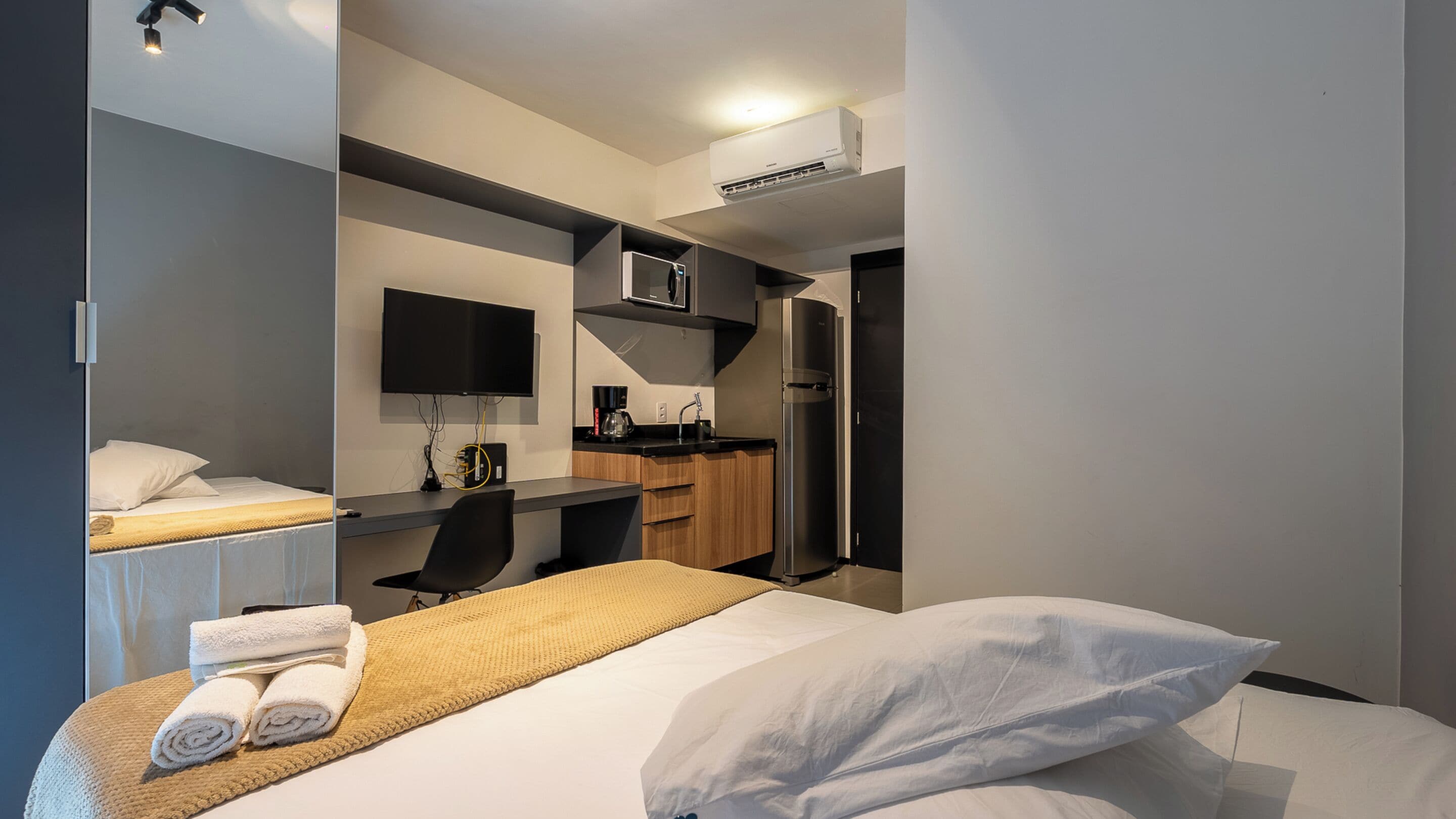 A modern hotel room with a bed, a desk, a flat-screen TV, a microwave, and a refrigerator.
