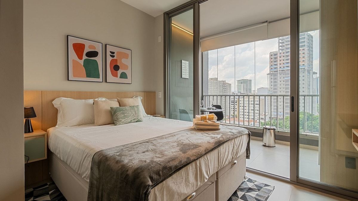 Et moderne hotelværelse med en stor seng, en balkon med udsigt over byen og abstrakt kunst på væggen.