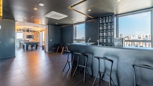 Uma área de bar moderna com vista para a cidade, mesa de bilhar e banquetas.