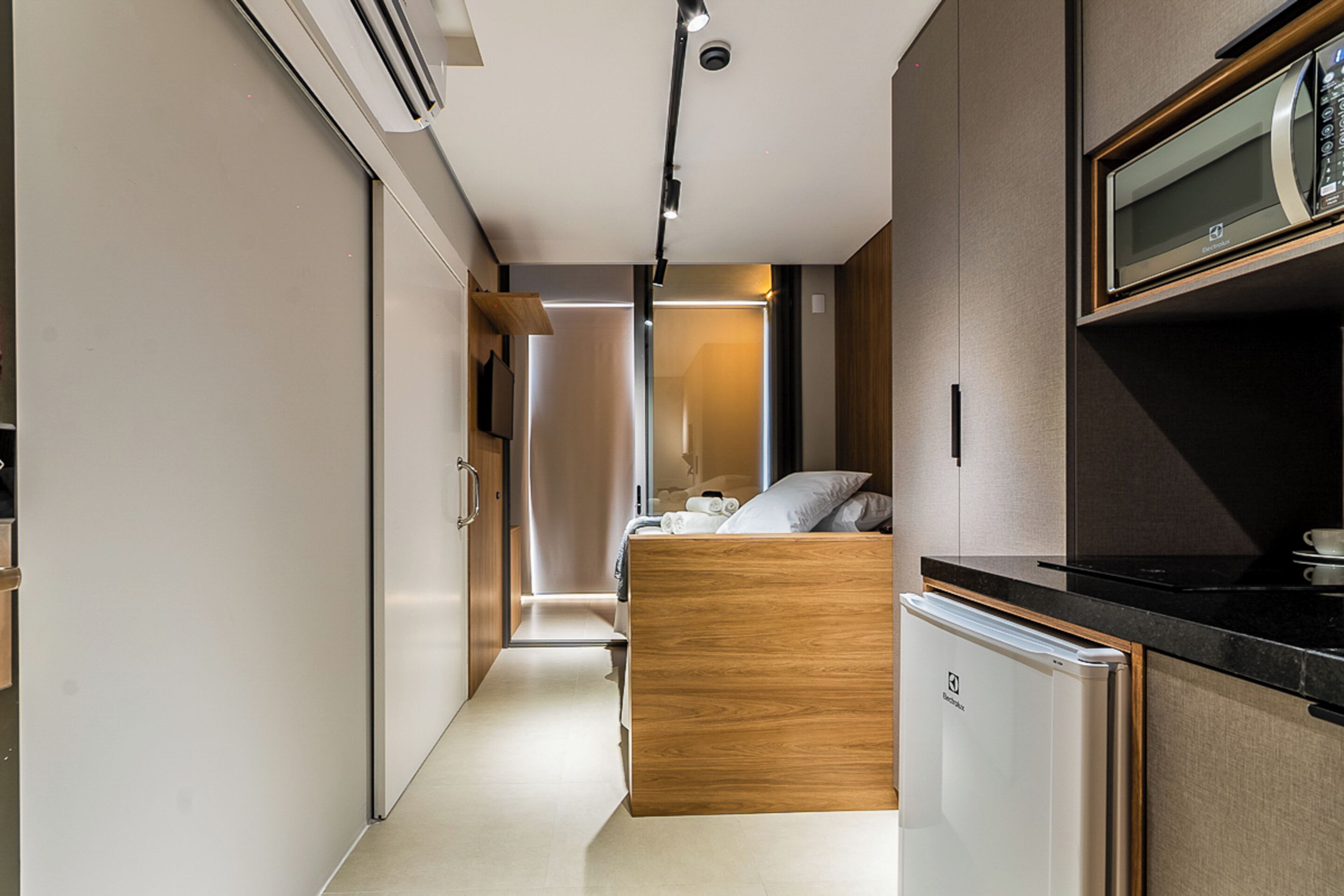 A compact, modern room with a kitchenette, a bed, and a small bathroom.