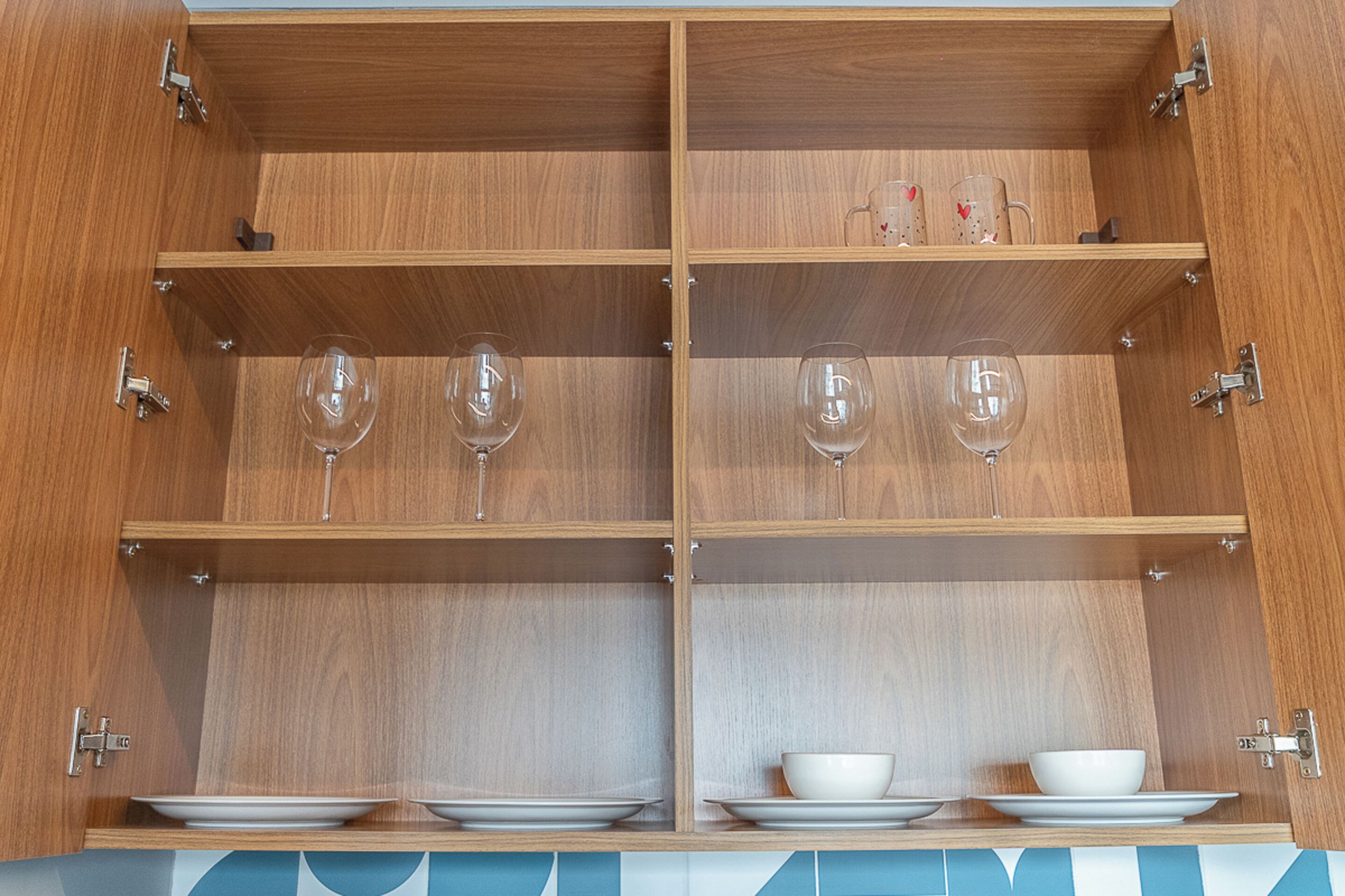 Un armario de madera con varios estantes, algunos con copas de vino y cuencos.