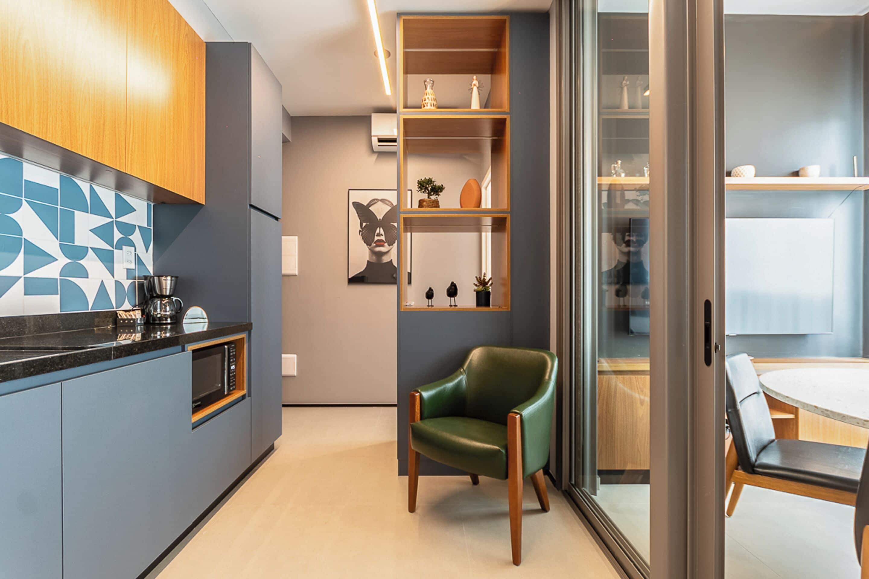 Eine moderne Küche mit integriertem Mikrowellenherd, einer Kaffeemaschine und einem Holzschrank. In der Ecke steht ein grüner Stuhl und ein Esstisch mit Stühlen.