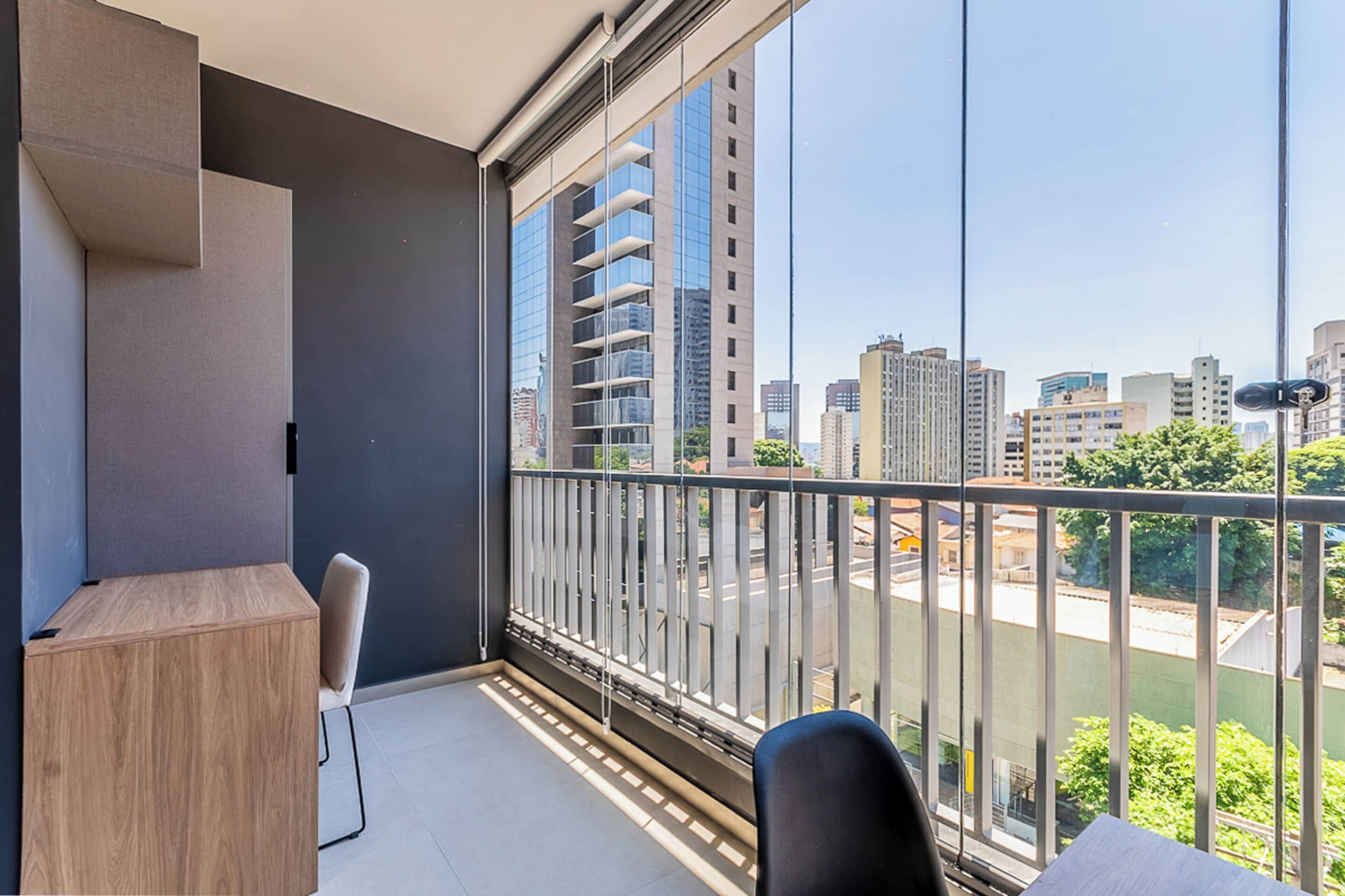 A balcony with a view of a cityscape, a wooden desk, and a chair.