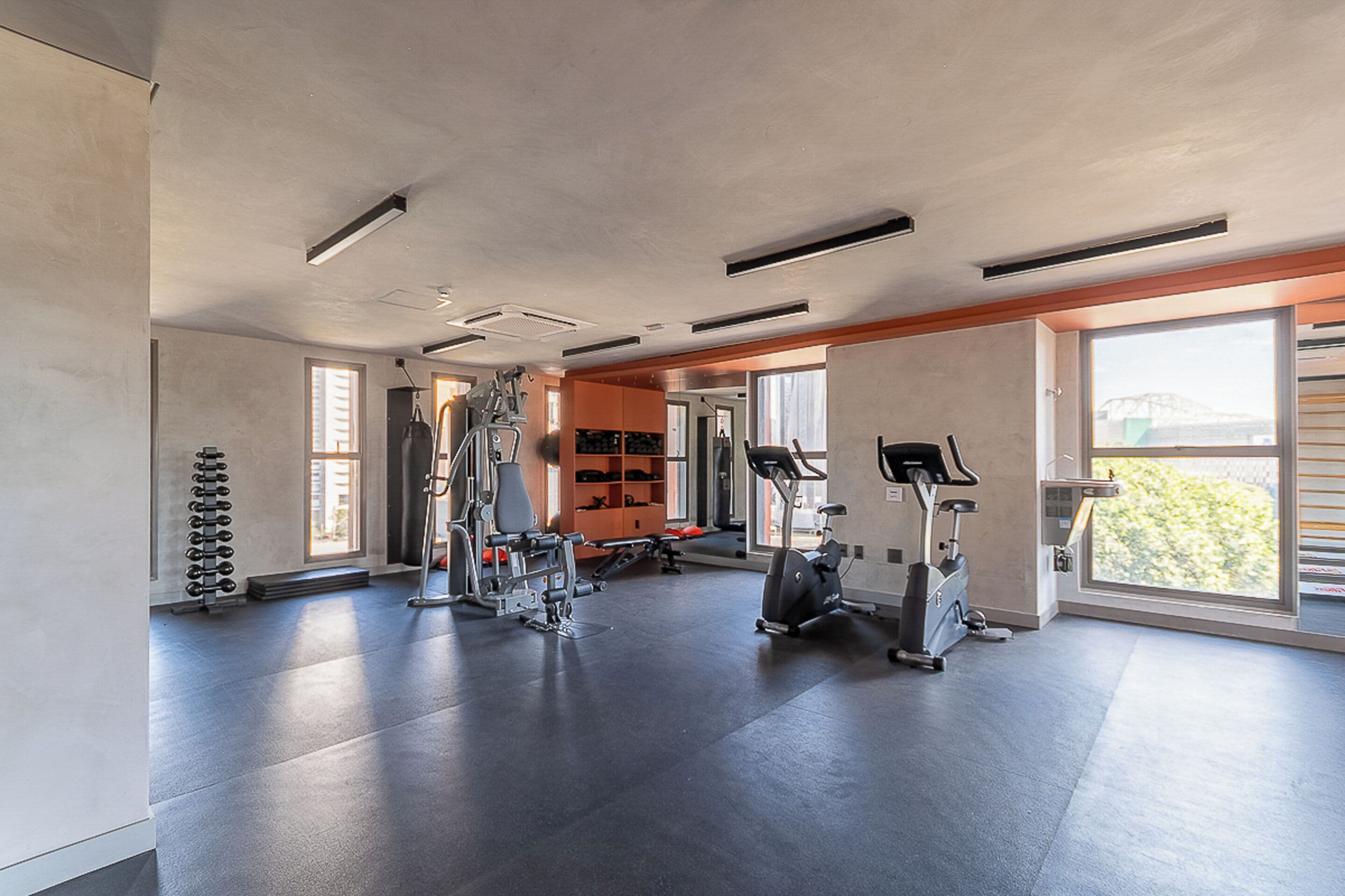 A gym with exercise equipment, large windows, and a concrete floor.