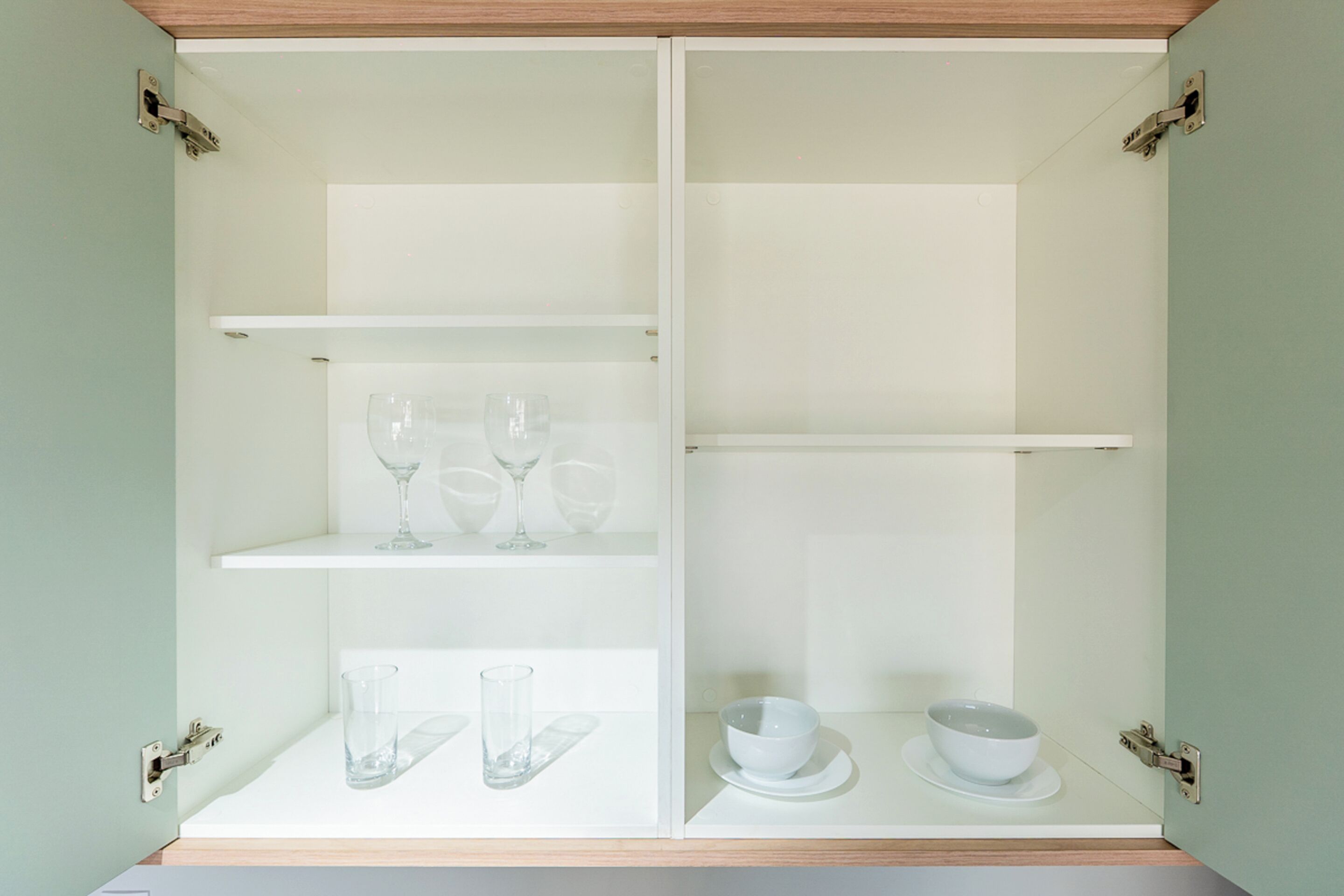 A white cabinet with two shelves, each holding clear glasses and a bowl on a plate.