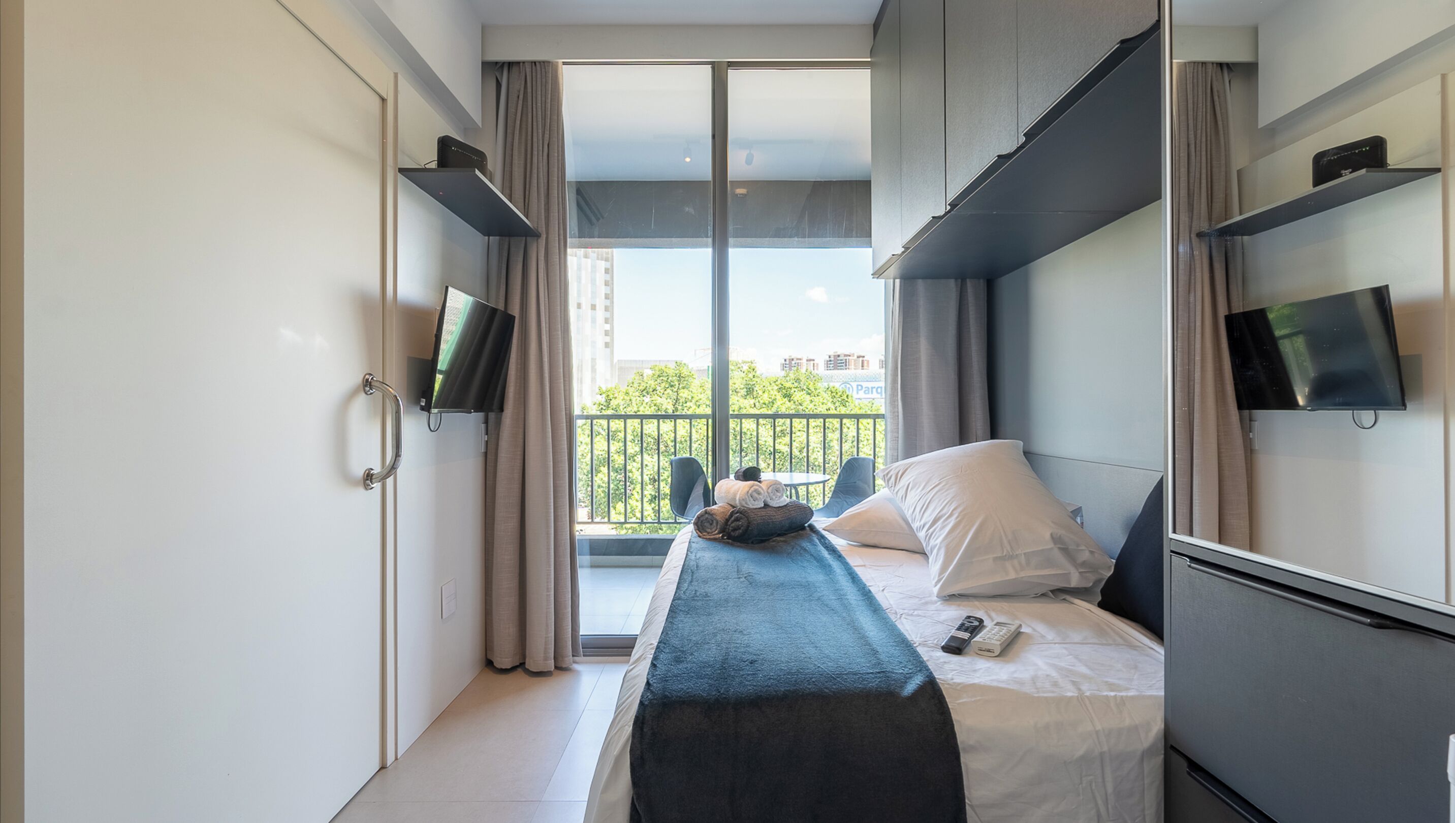Una habitación de hotel moderna con cama, televisión y balcón con vistas a la ciudad.