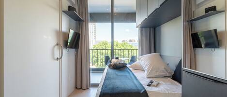 Una habitación de hotel moderna con cama, televisión y balcón con vistas a la ciudad.