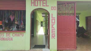 Entrada de hotel com uma porta vermelha e uma placa com o texto "HOTEL DO LOKER".