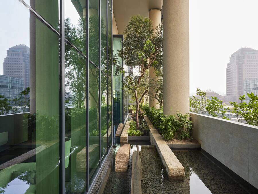 A modern building with large glass windows, a water feature, and greenery.