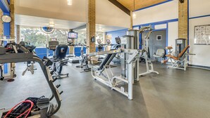 Una palestra con diverse macchine per esercizi, un ventilatore a soffitto e ampie finestre.