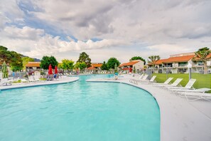 En swimmingpool med solstolar och parasoller, omgiven av byggnader med röda tak.
