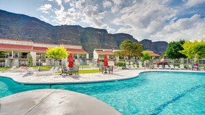 A swimming pool with lounge chairs and umbrellas, surrounded by buildings with red roofs, set against a mountainous backdrop. - Lovely Crescent Bar Condo w/ Community Amenities! (Quincy)