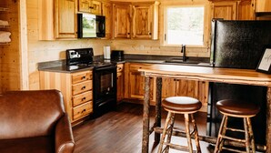 A wooden cabin-style kitchen with a wooden countertop, a stove, a sink, and two stools. - The Elk Cabin - Hidden Acres Cabins (Bethany)