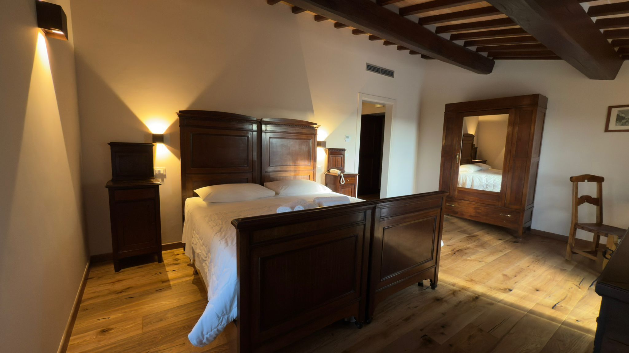 Un dormitorio con cama de madera, mesitas de noche, un espejo y suelo de madera.