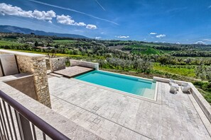 Una piscina con baldosas de piedra y vista a un paisaje verde.