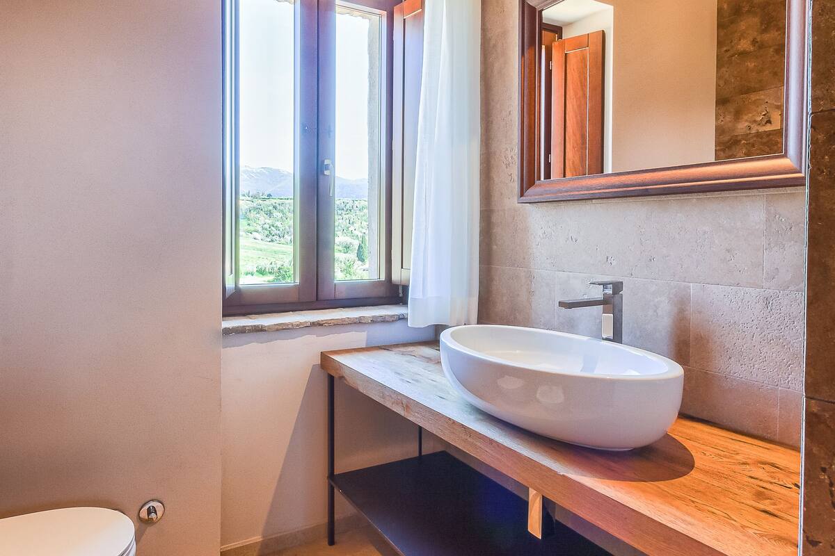 Un baño con un ventanal amplio, un lavamanos blanco y un espejo.