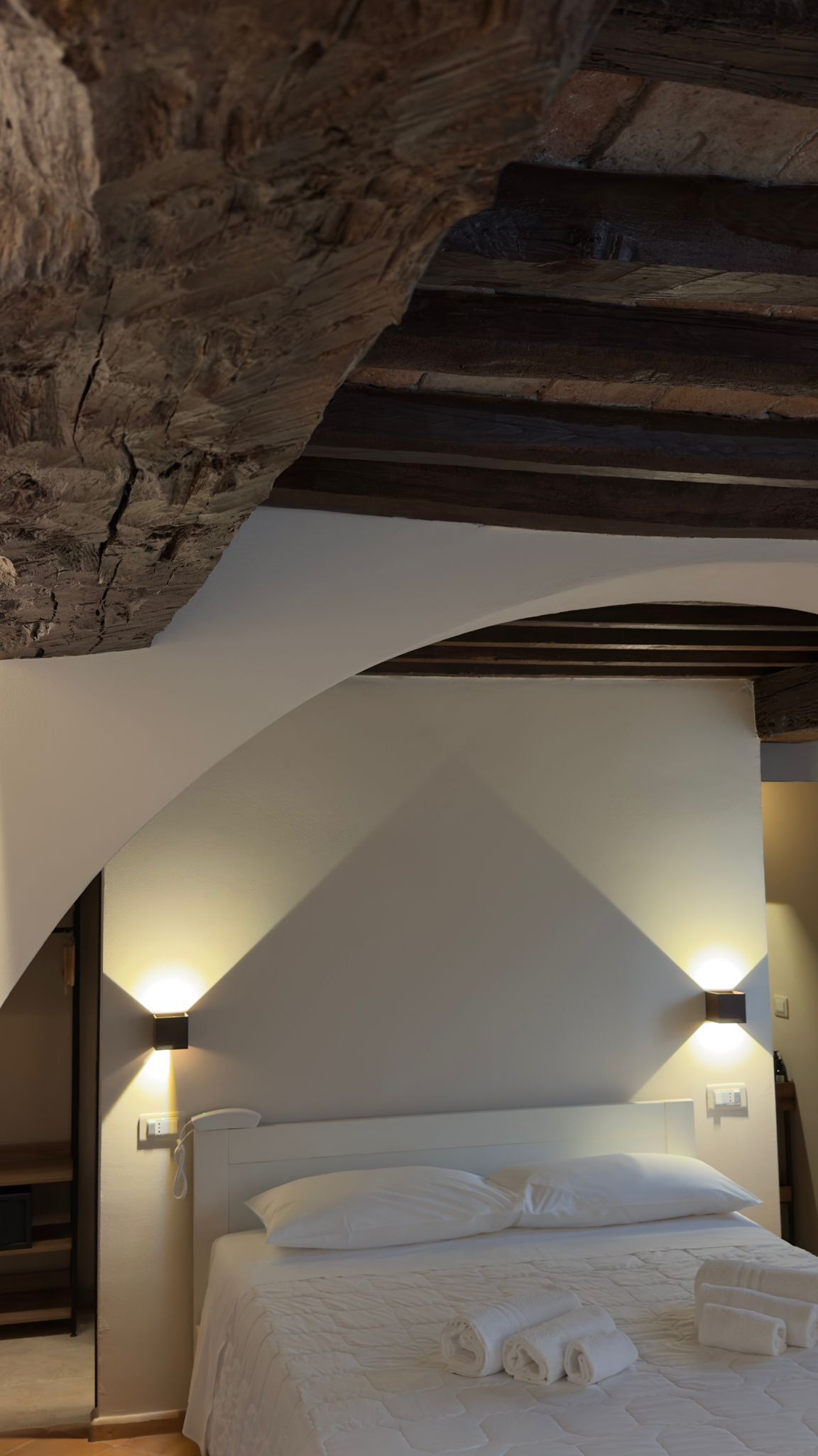 A bedroom with a bed, two wall-mounted lights, and a wooden ceiling.