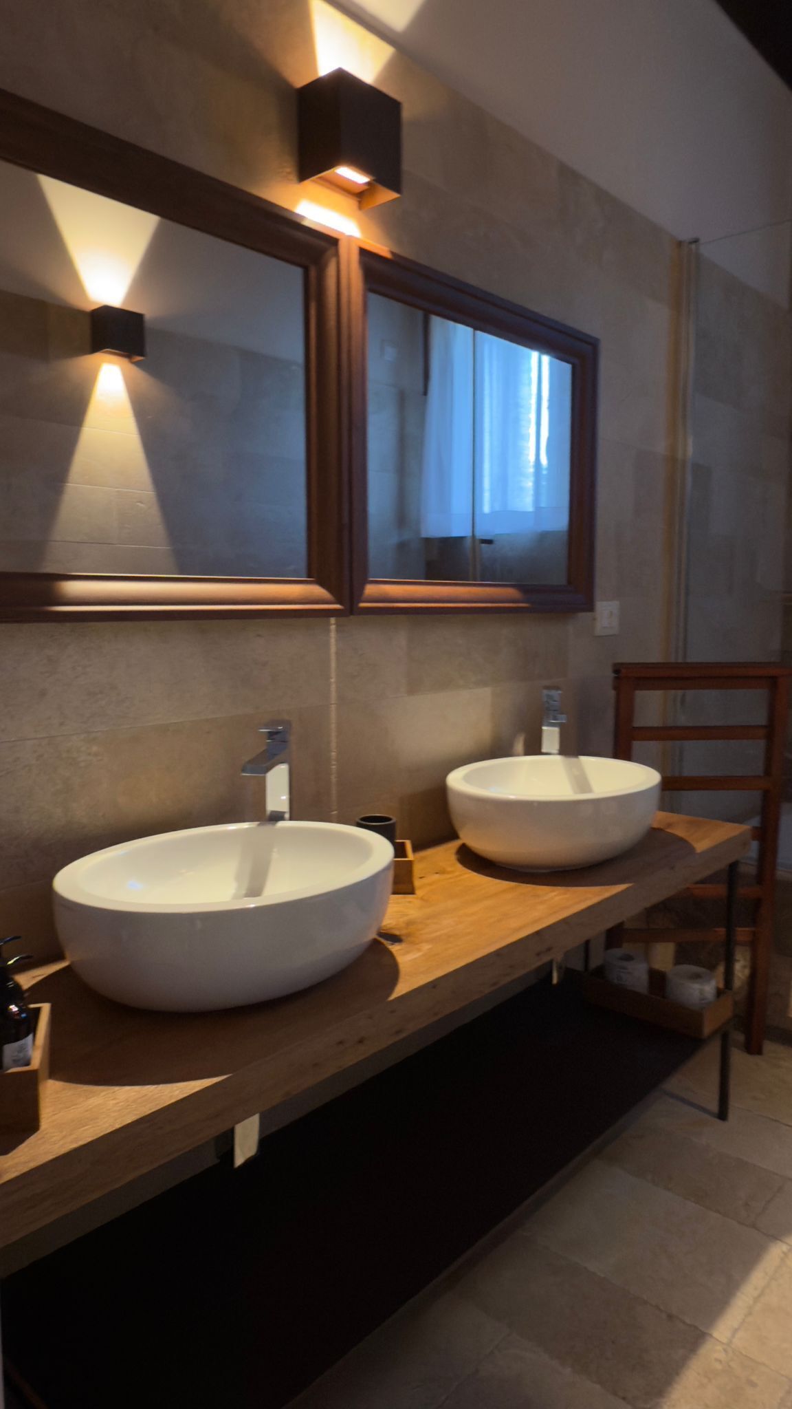 A bathroom with two large white sinks, a wooden vanity, and a mirror with integrated lighting.
